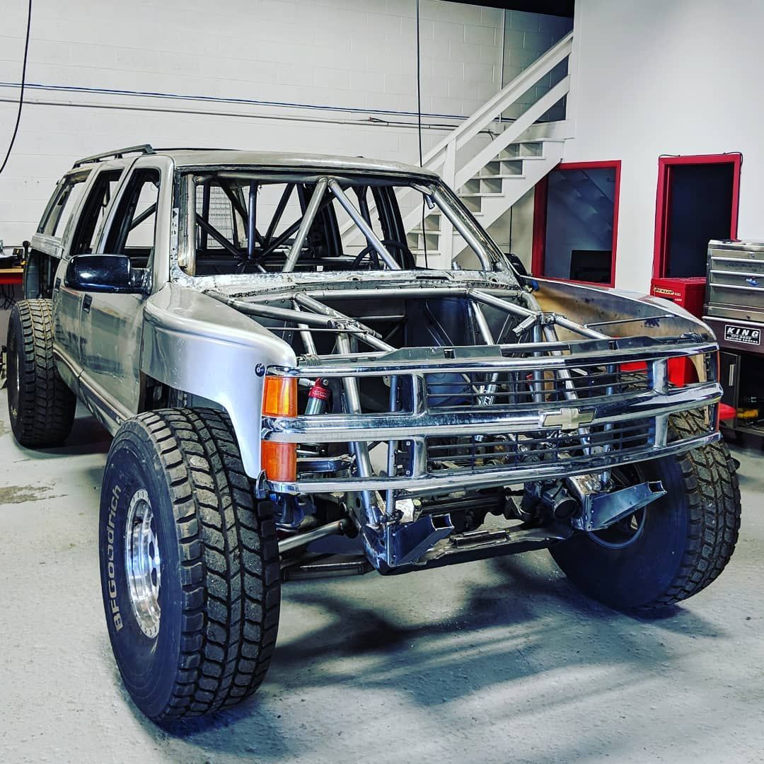 A silver jeep is parked in a garage with stairs in the background