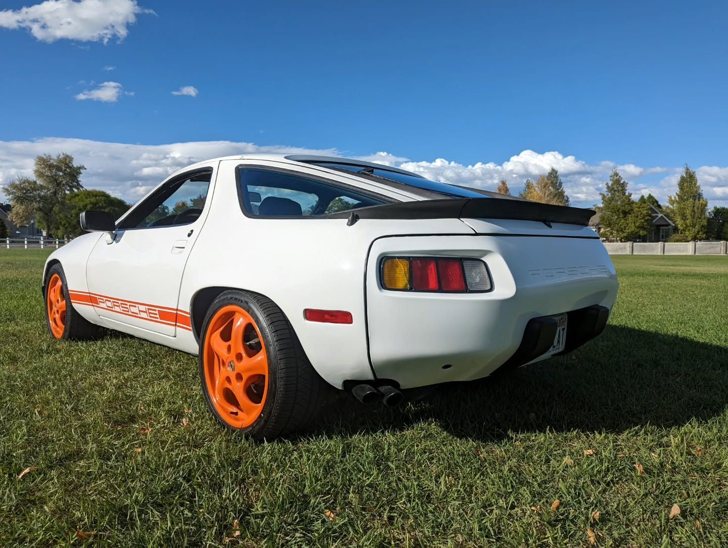 A white car with orange wheels is parked in a grassy field.