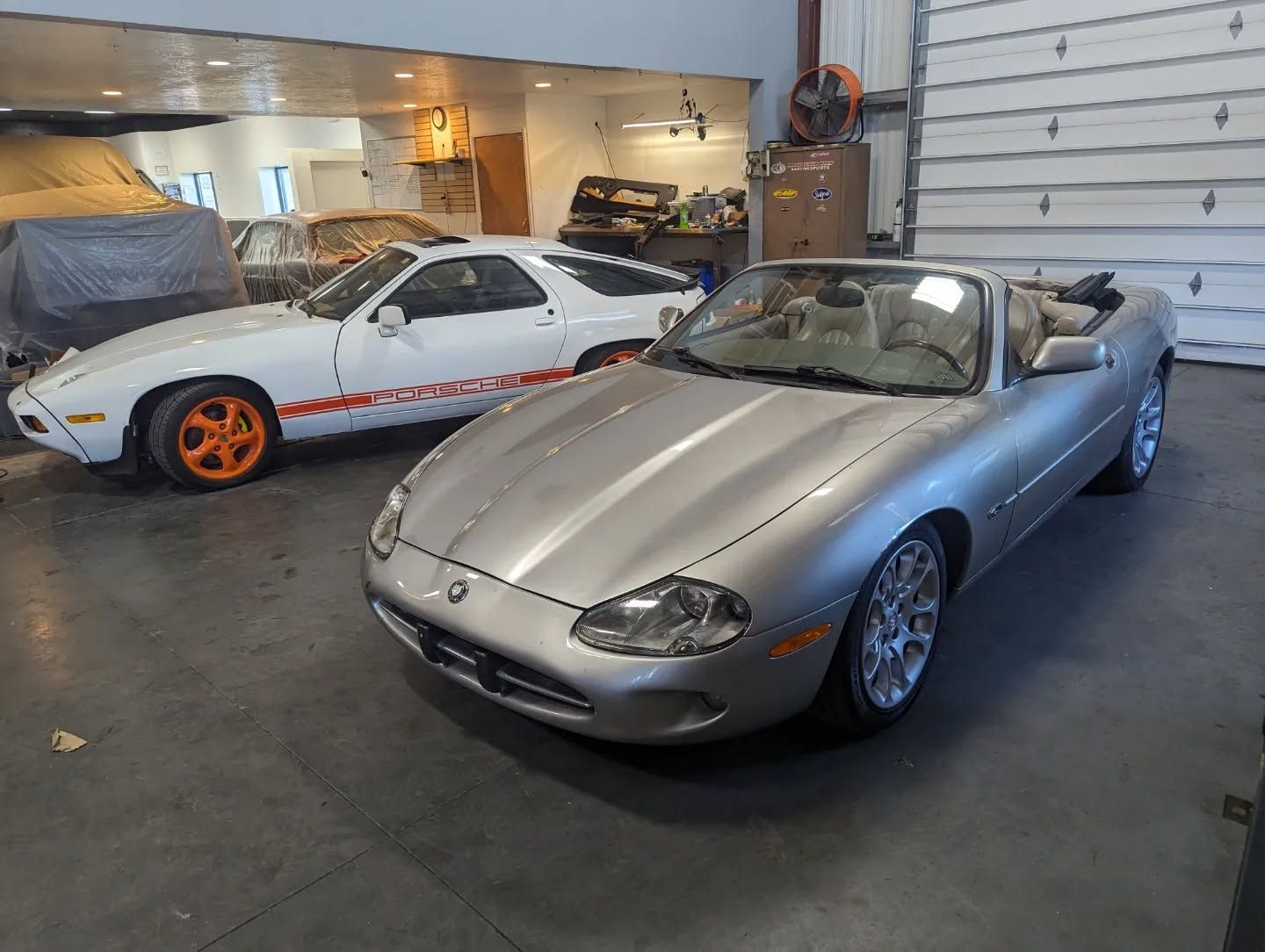 A silver sports car is parked next to a white sports car in a garage.
