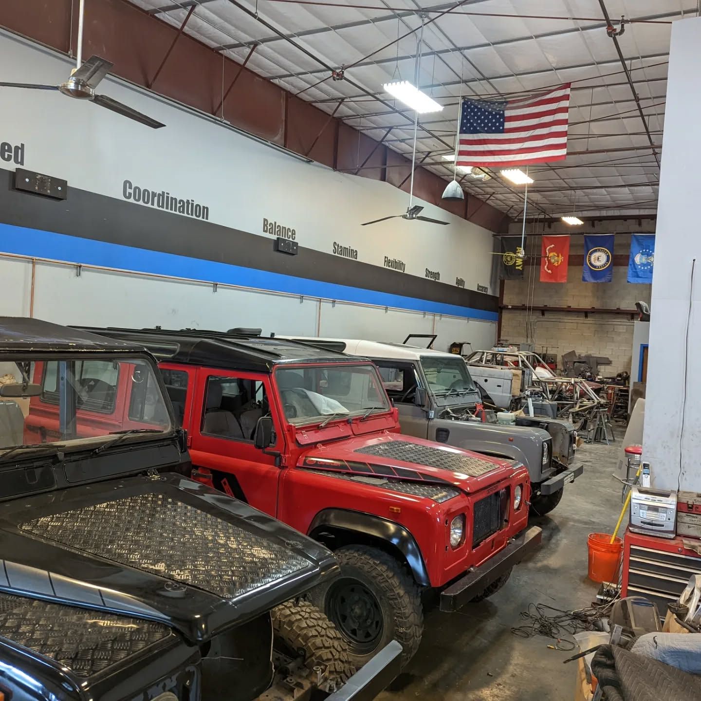 A row of jeep 's are parked in a garage with an american flag hanging from the ceiling