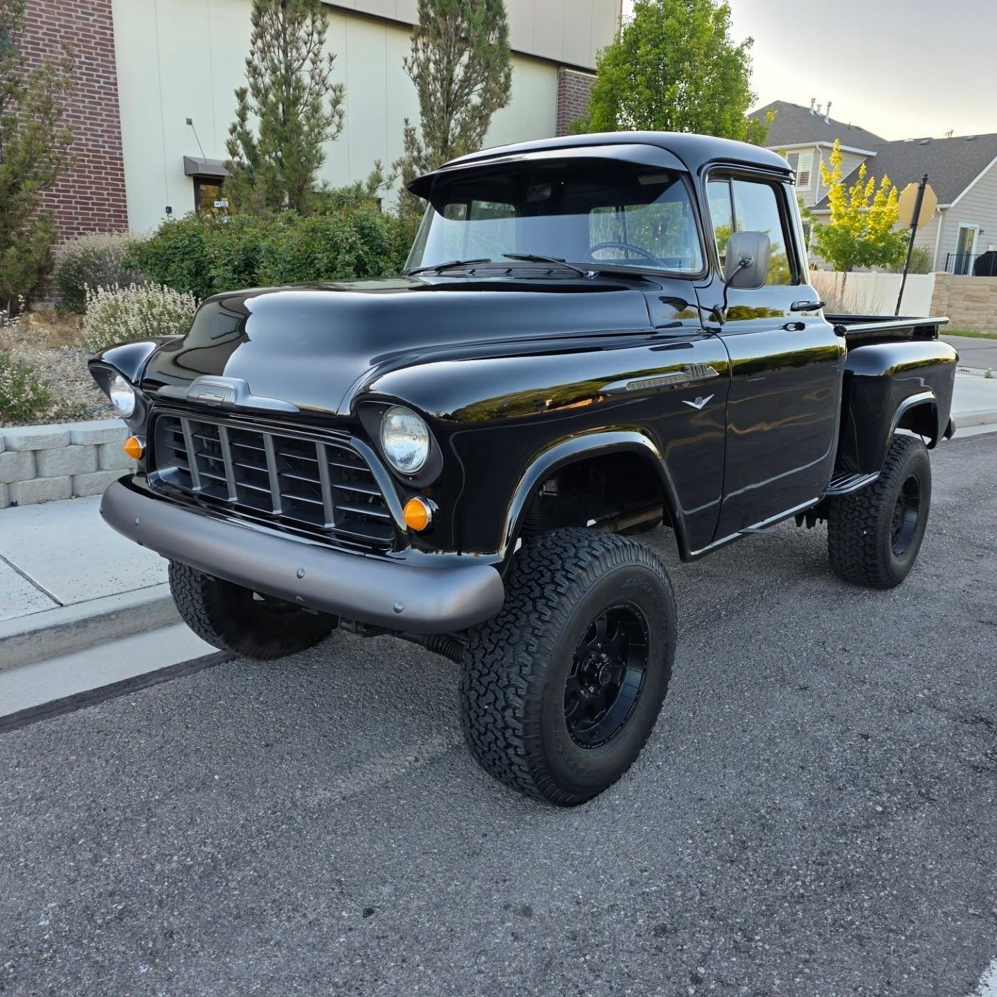 Black vintage Chevrolet pickup truck with large off-road tires parked on pavement.
