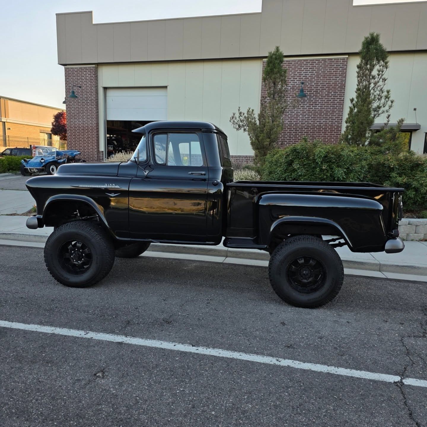 Black, lifted vintage pickup truck parked on the street. Building in the background.
