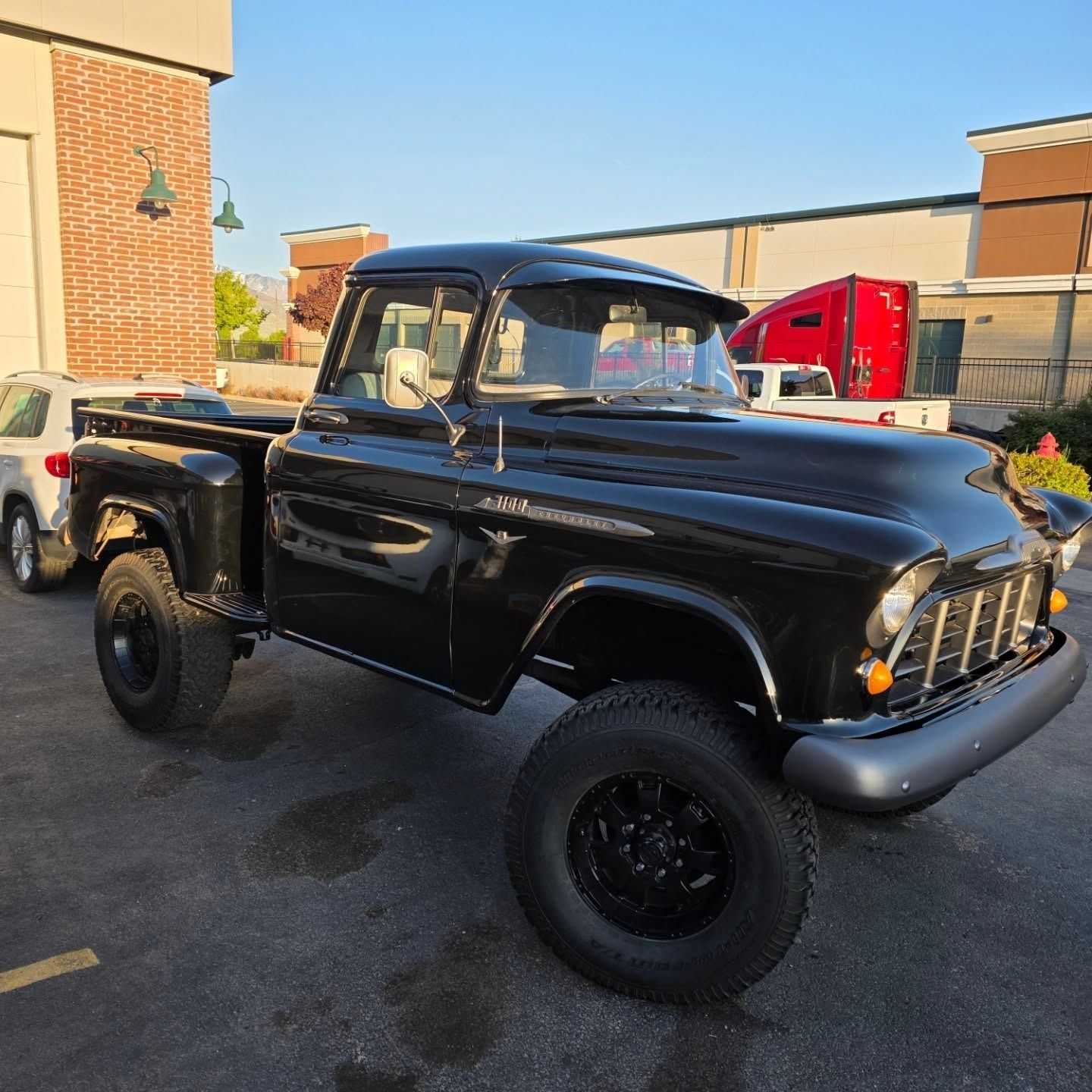 Black vintage Chevrolet pickup truck, parked in a lot. Black tires and rims.