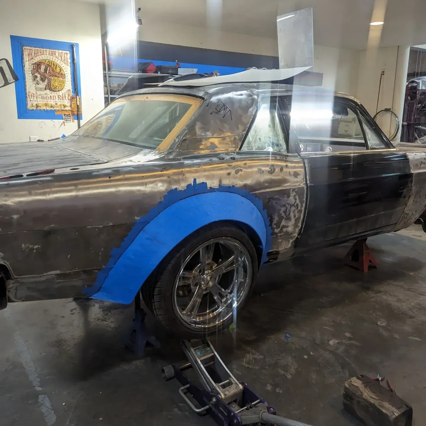 Classic car in a garage, blue fender flares, on jack stands, being worked on.