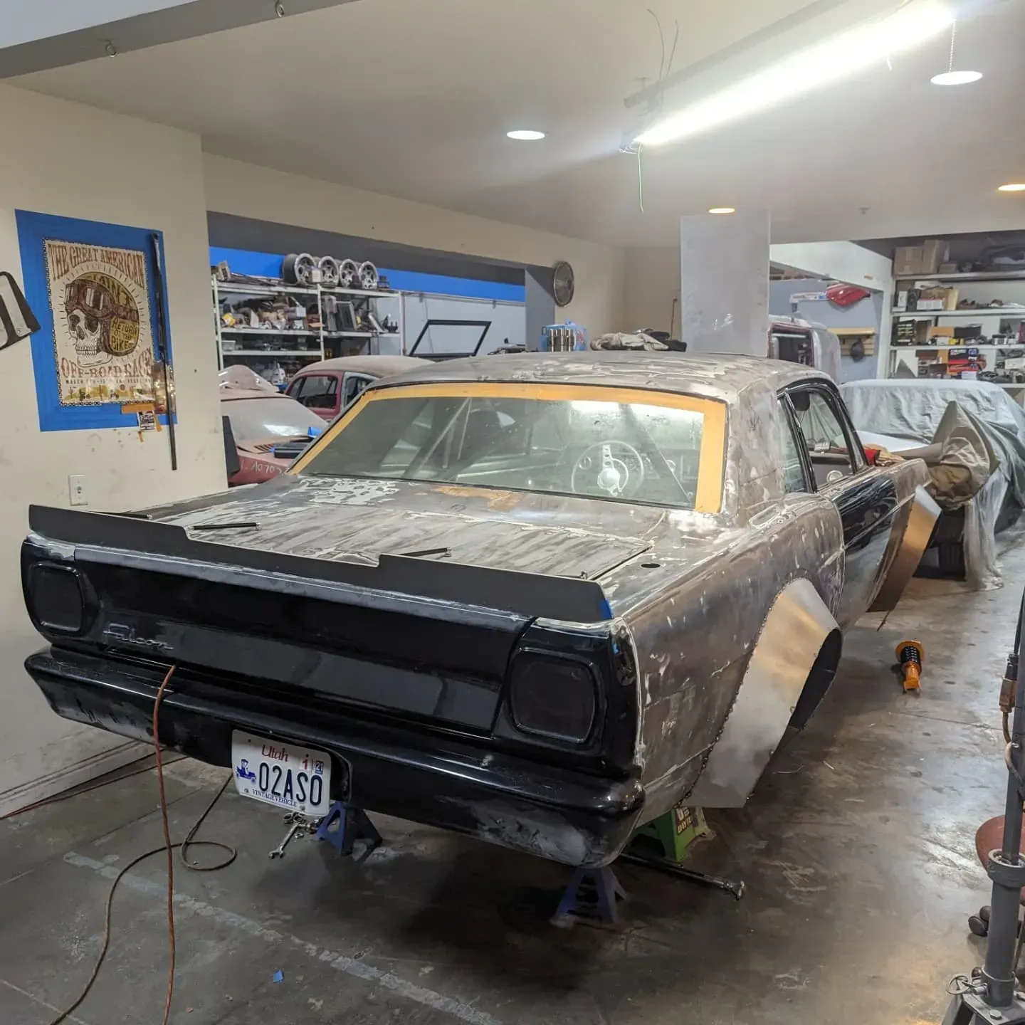 A classic, dark-colored car in a garage, undergoing restoration with panels removed, on jack stands.