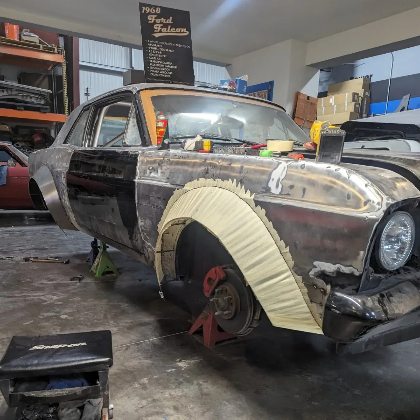 A classic car in a garage is being worked on; it has custom wheel arches and primer.