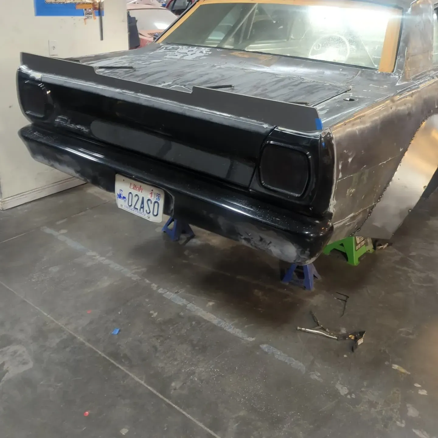 Black classic car rear with spoiler, in a garage. License plate visible.