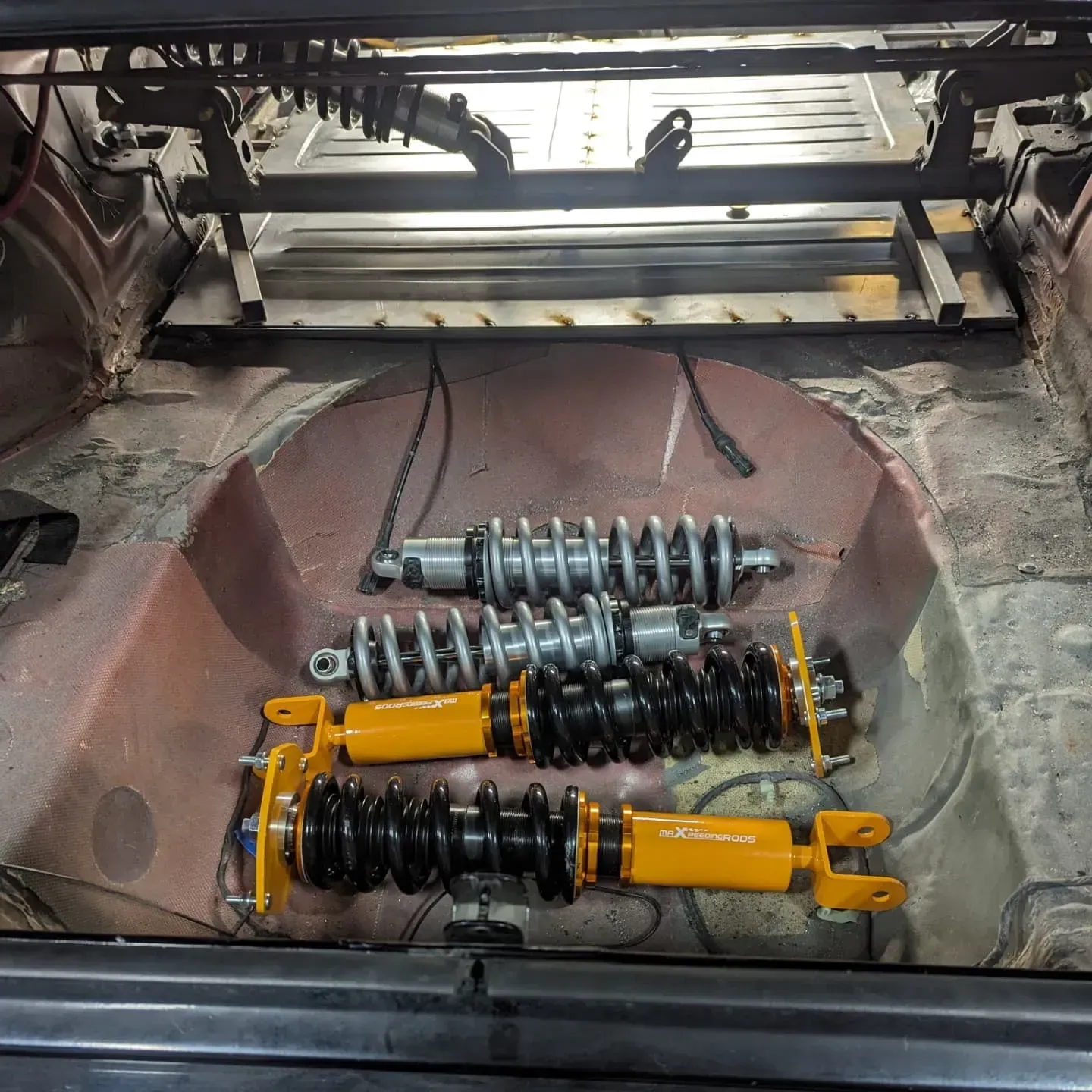 Two sets of coilover shock absorbers inside a car's trunk. Yellow and silver struts visible.
