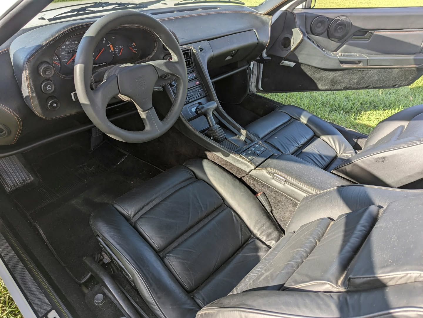 Black leather interior of a vintage Porsche car; black steering wheel and dashboard visible.