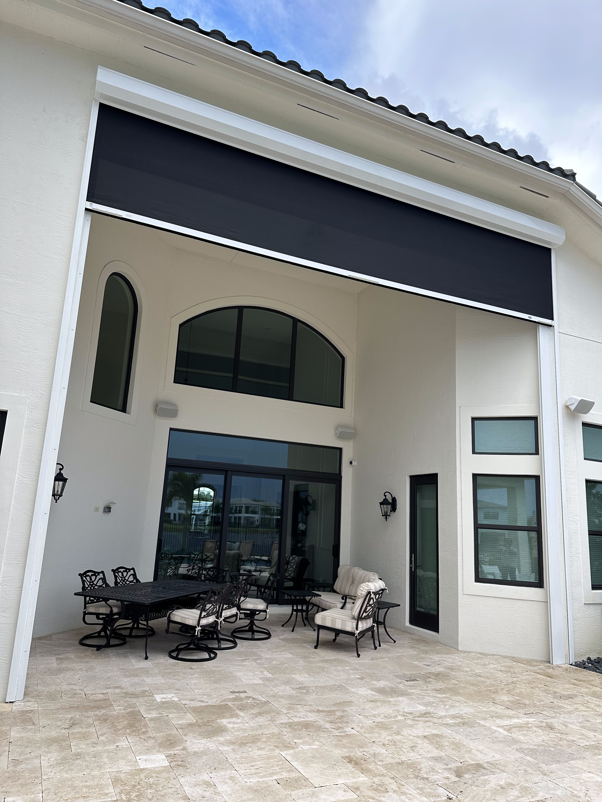 Black retractable awning over patio with outdoor furniture. White stucco building, sunny sky.
