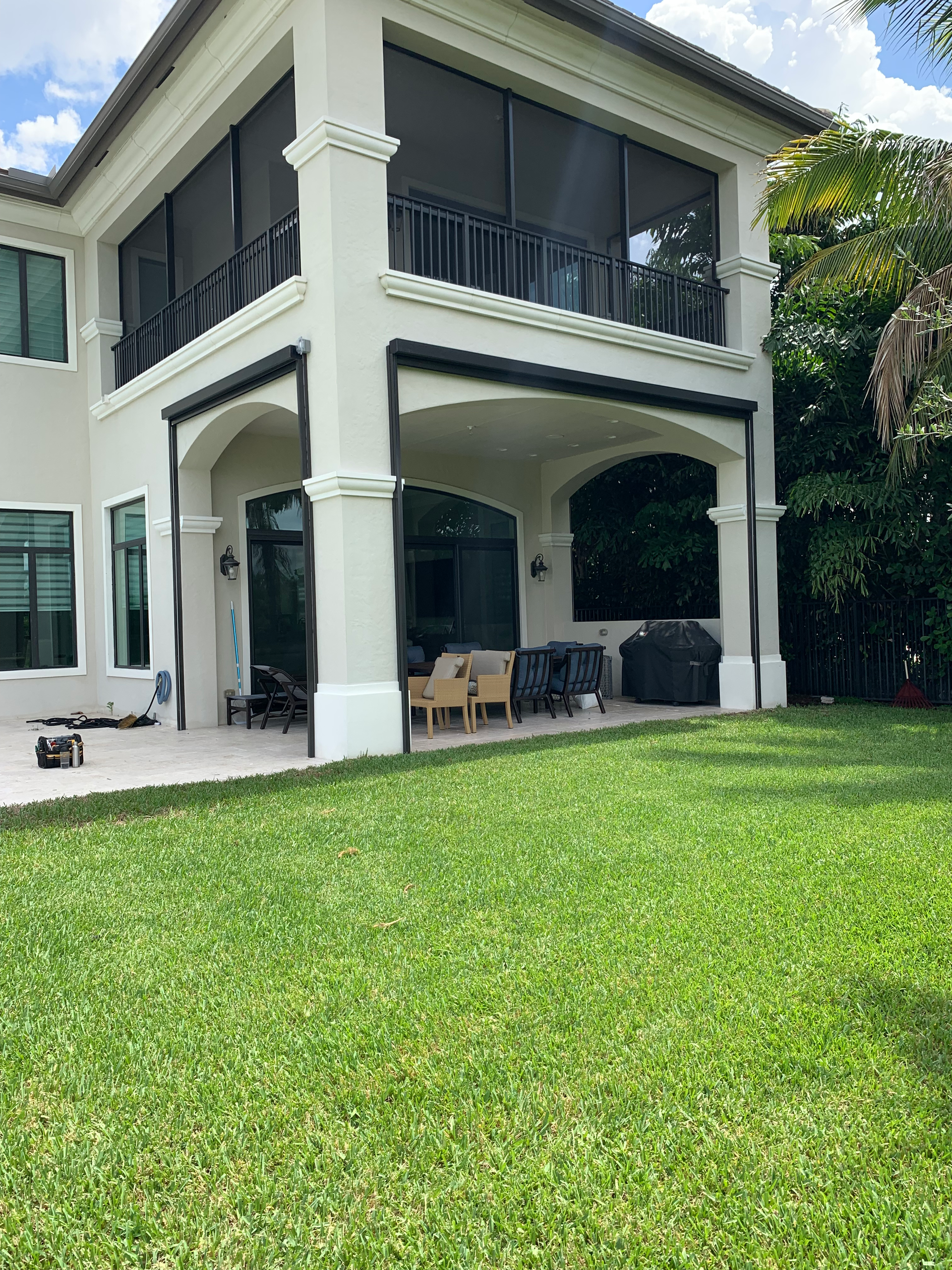 Two-story house with a screened-in balcony, light-colored exterior, and a green lawn.
