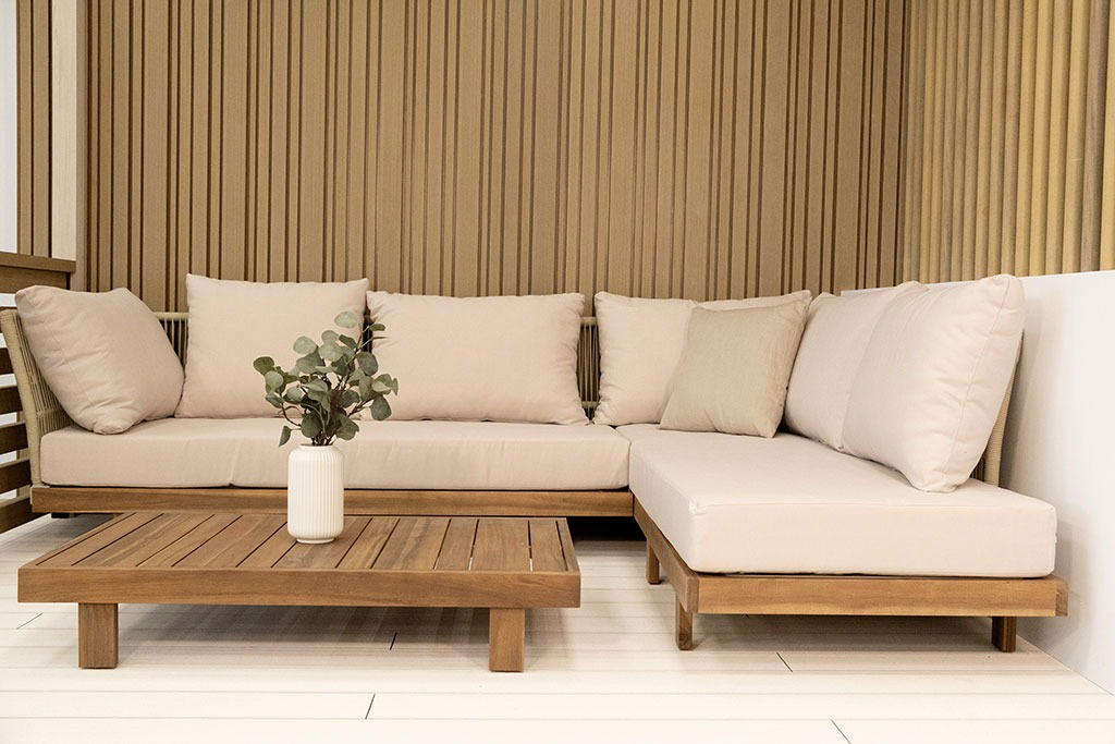 L-shaped outdoor sofa with beige cushions, wooden coffee table, and backdrop of draped fabric.