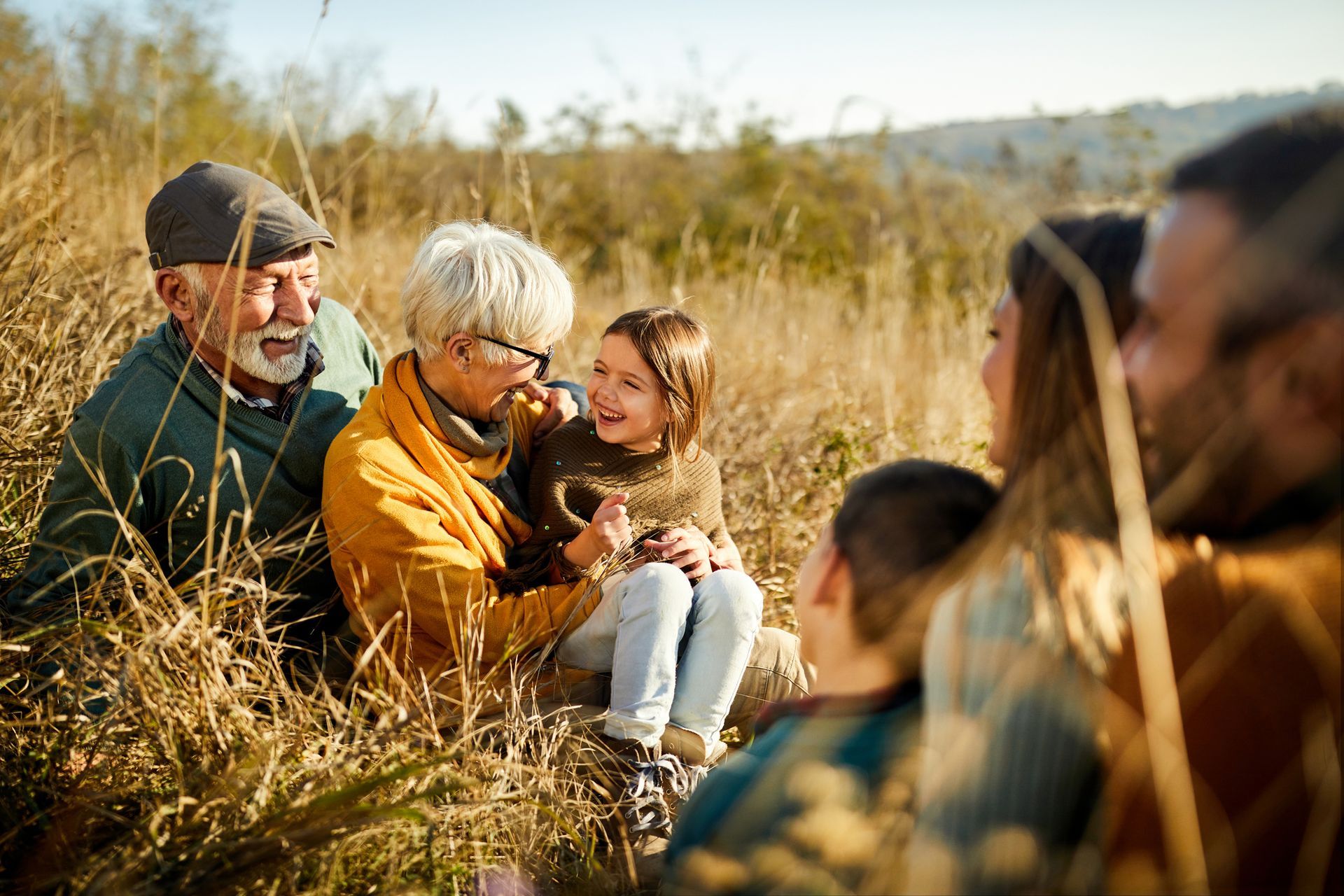 Family sitting in tall grass, smiling at each other in a sunny field.