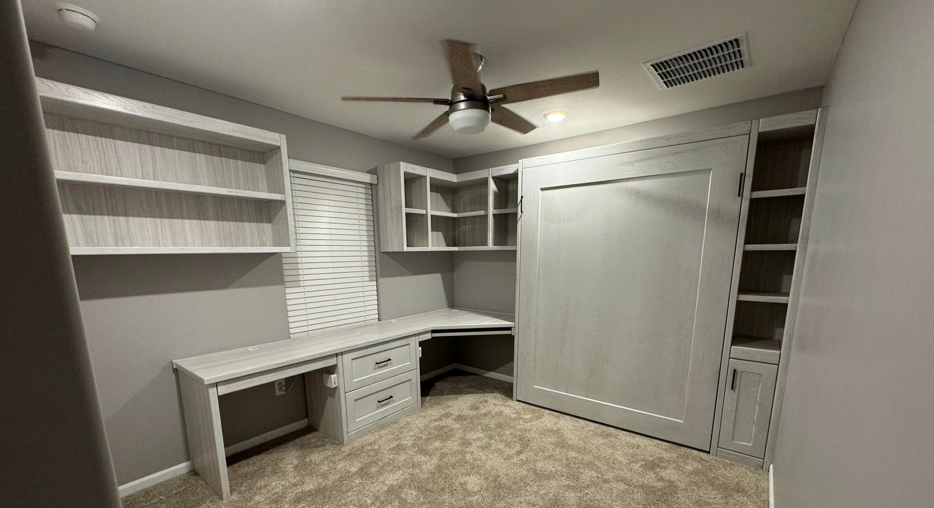 A room with a desk , shelves , and a ceiling fan.