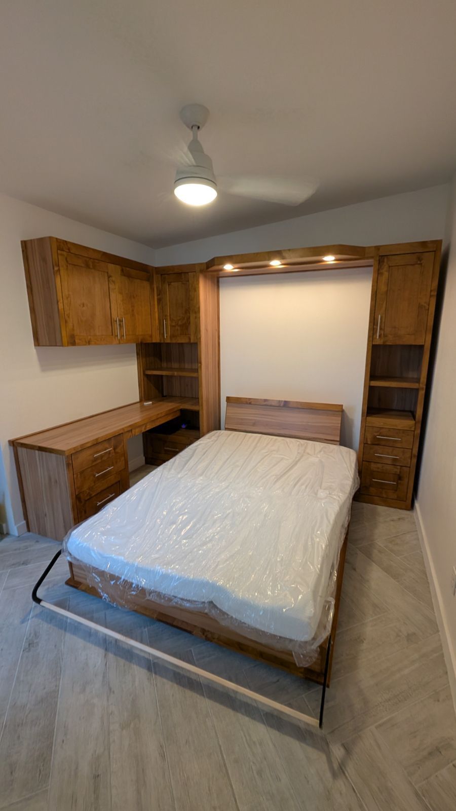 A bedroom with a bed , desk , cabinets and a ceiling fan.