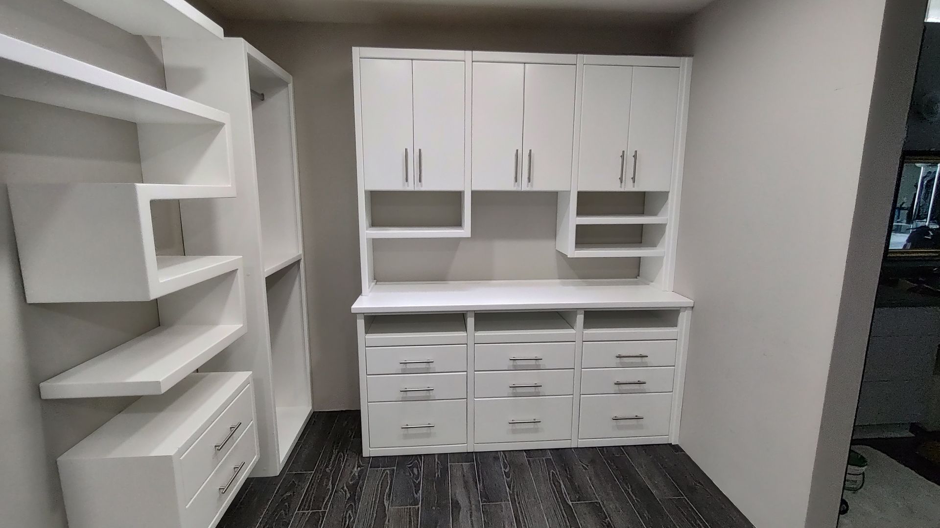 A room with white cabinets , shelves , drawers and a desk.