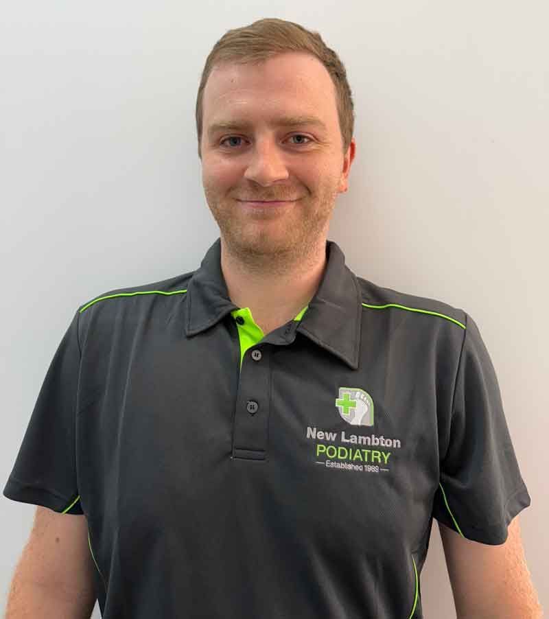 A man with a beard is wearing a black polo shirt and smiling.