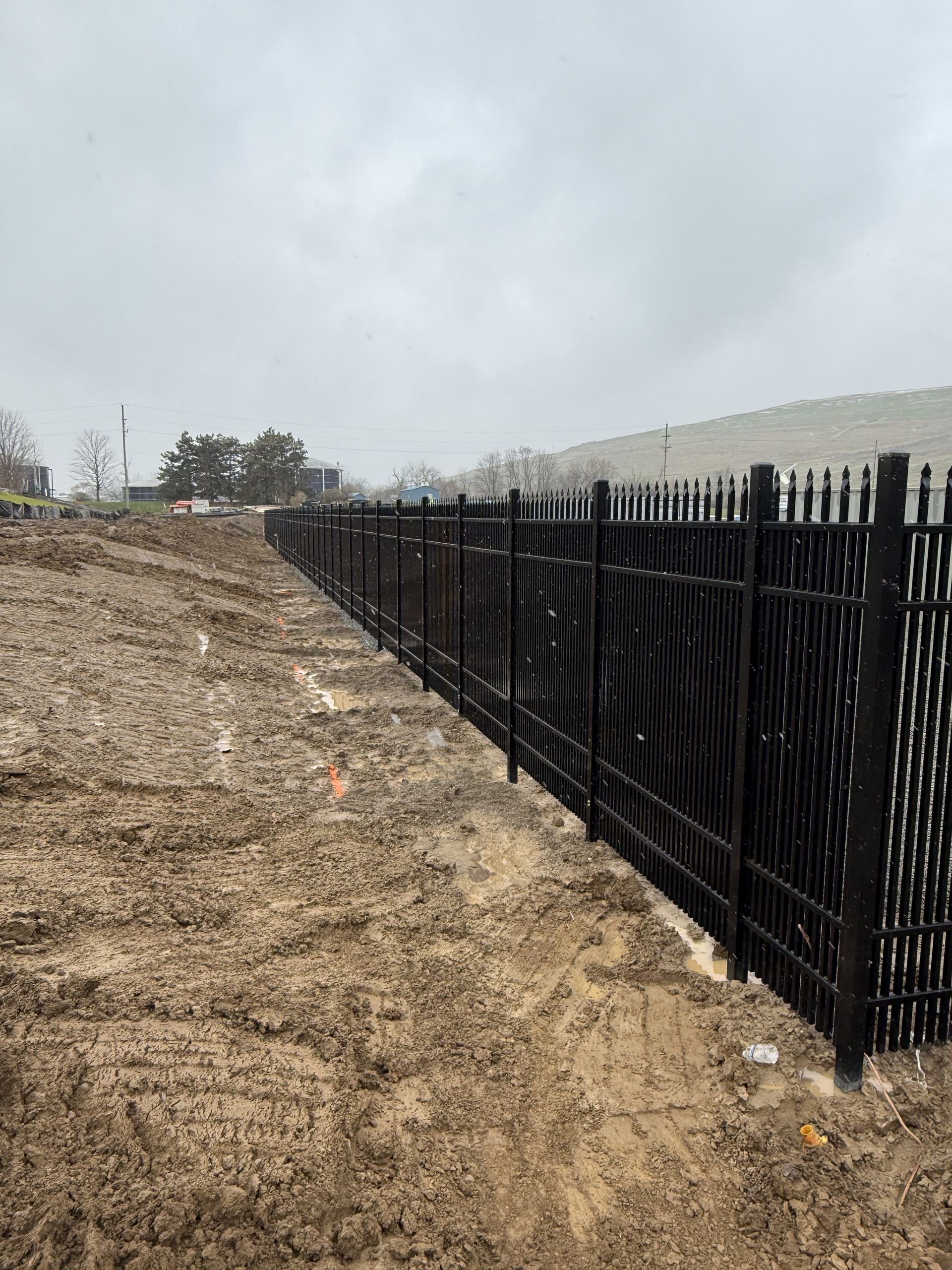 Black metal fence bordering muddy ground on a cloudy day.