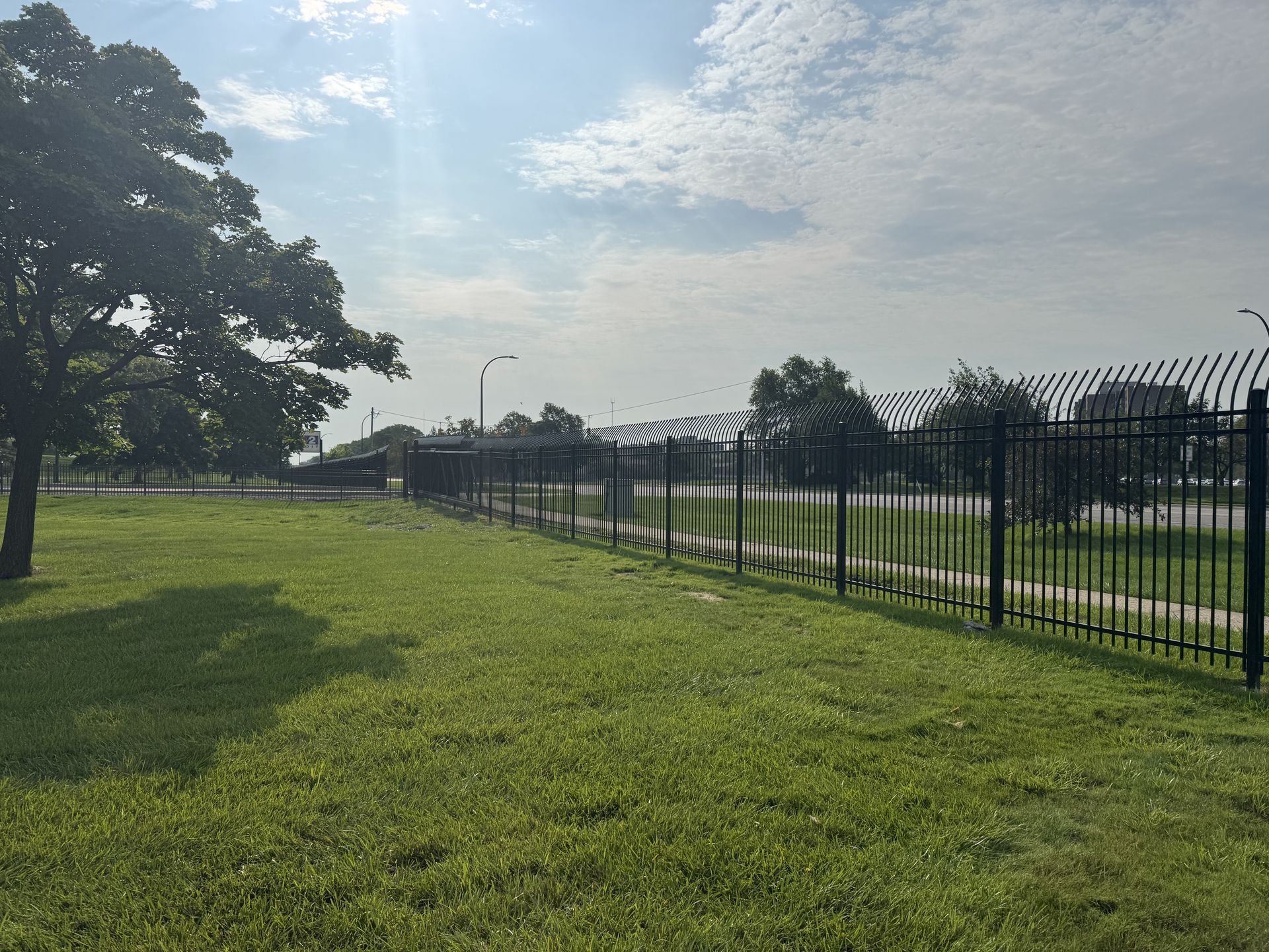 Black fence topped with razor wire along grassy area on a sunny day.