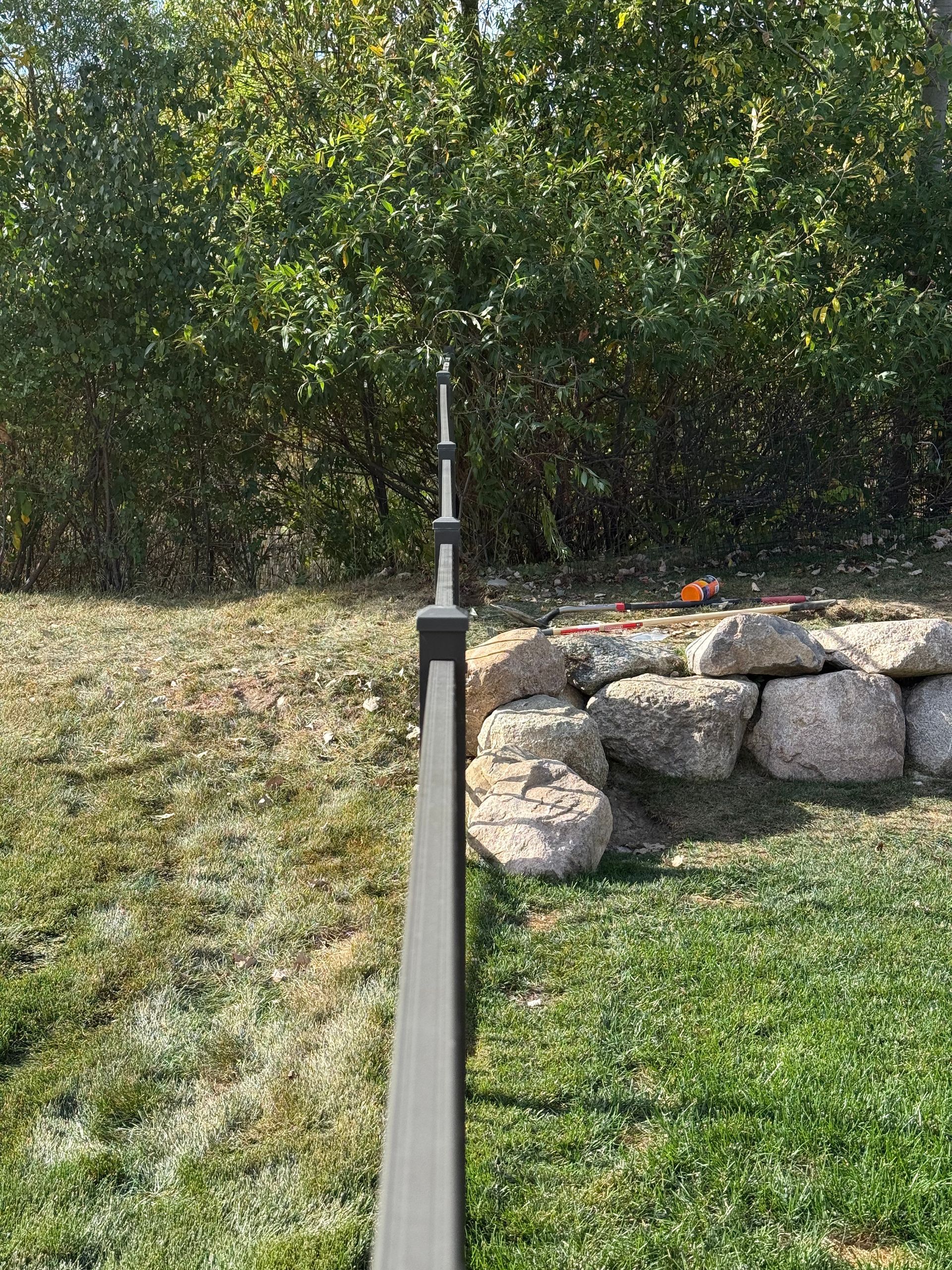 Dark gray fence with finials along green lawn and a rock wall, with green foliage in background.