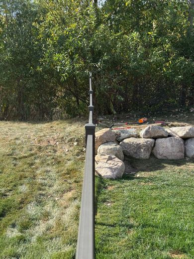 Dark gray fence with finials along green lawn and a rock wall, with green foliage in background.