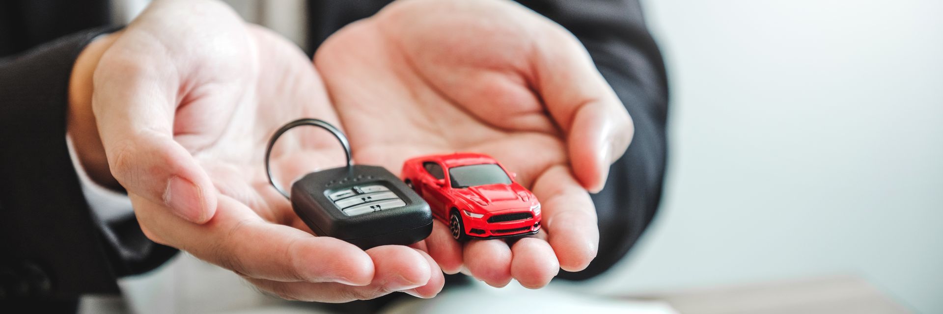 Hands holding a car key fob and a miniature red car.