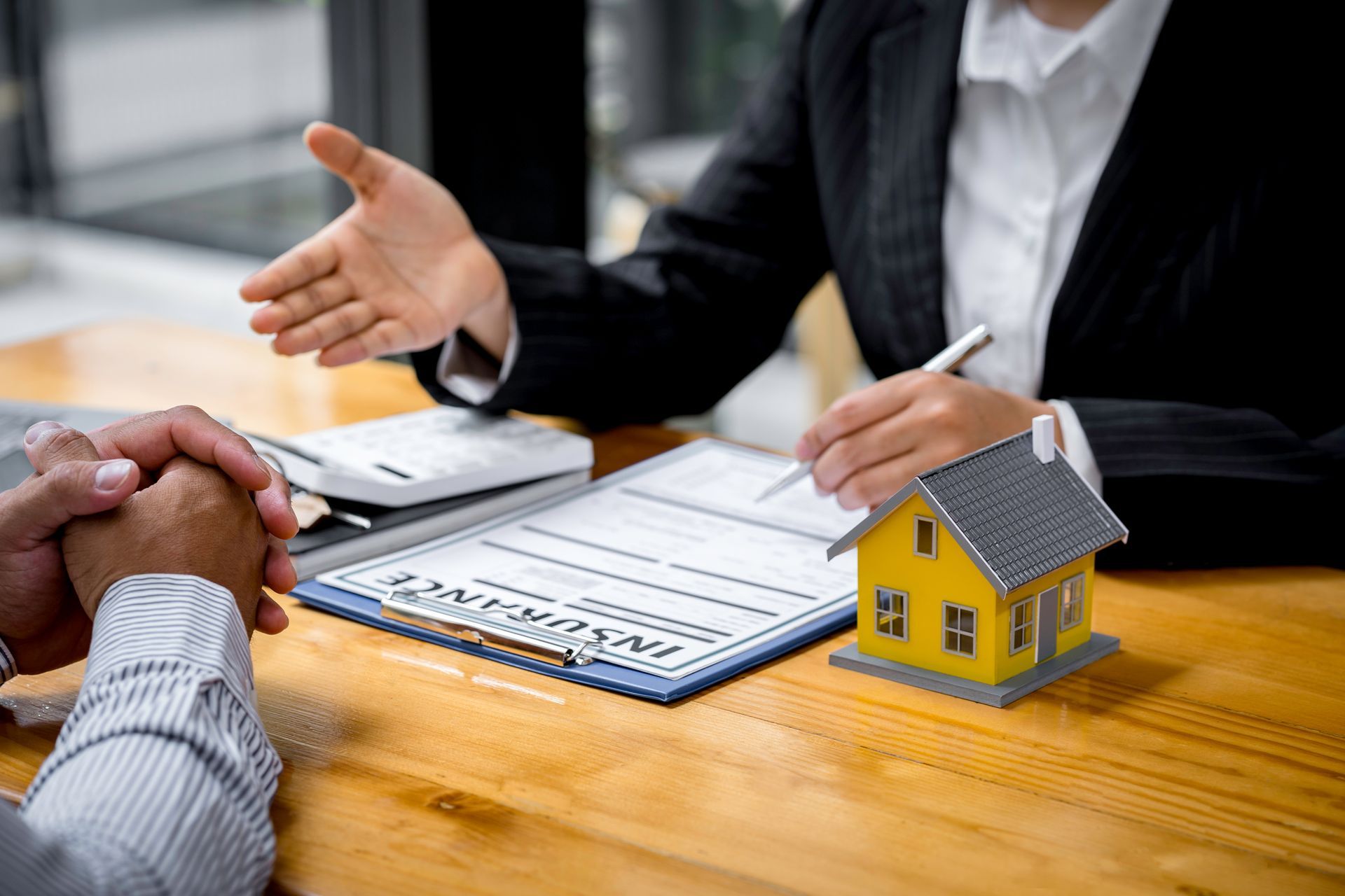 Person gesturing towards insurance paperwork and model house at a table.