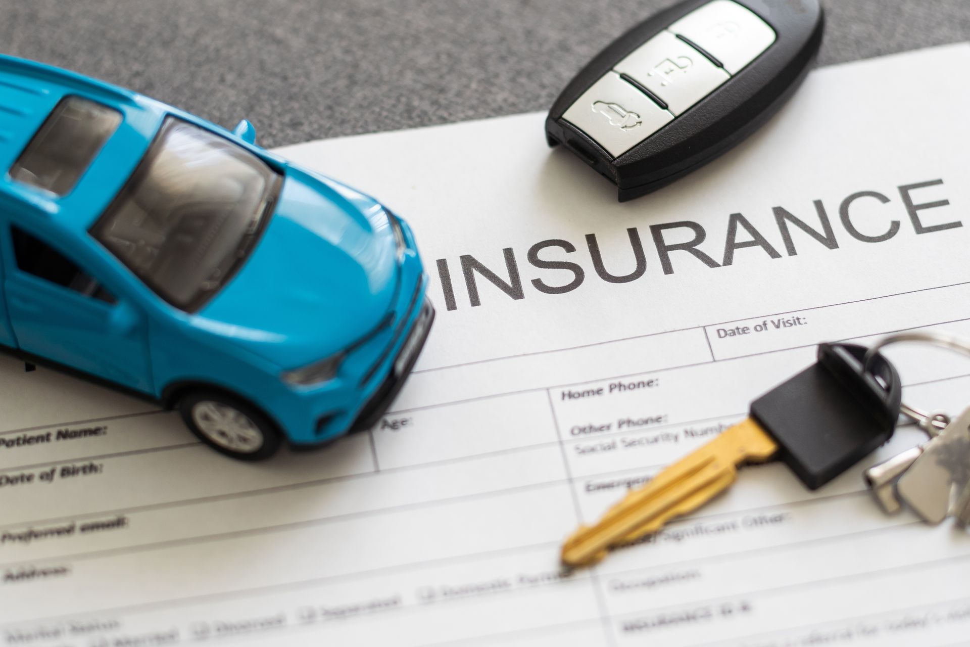 Blue toy car, key, and car key fob on an insurance document.