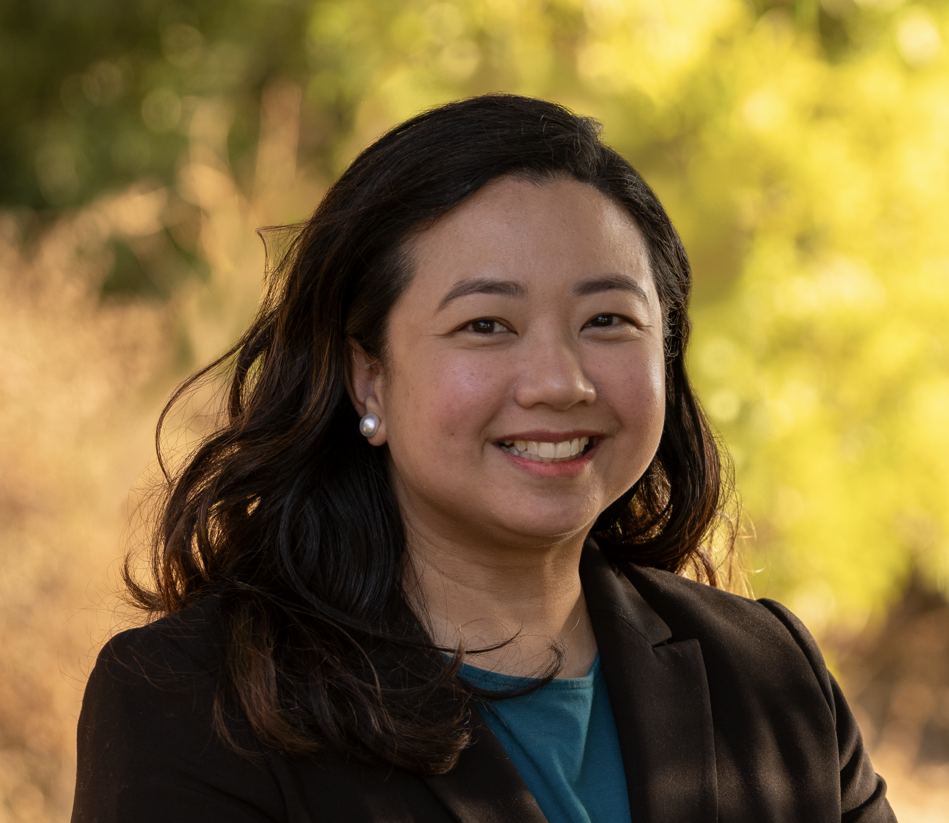 A woman in a black jacket and blue shirt is smiling for the camera.