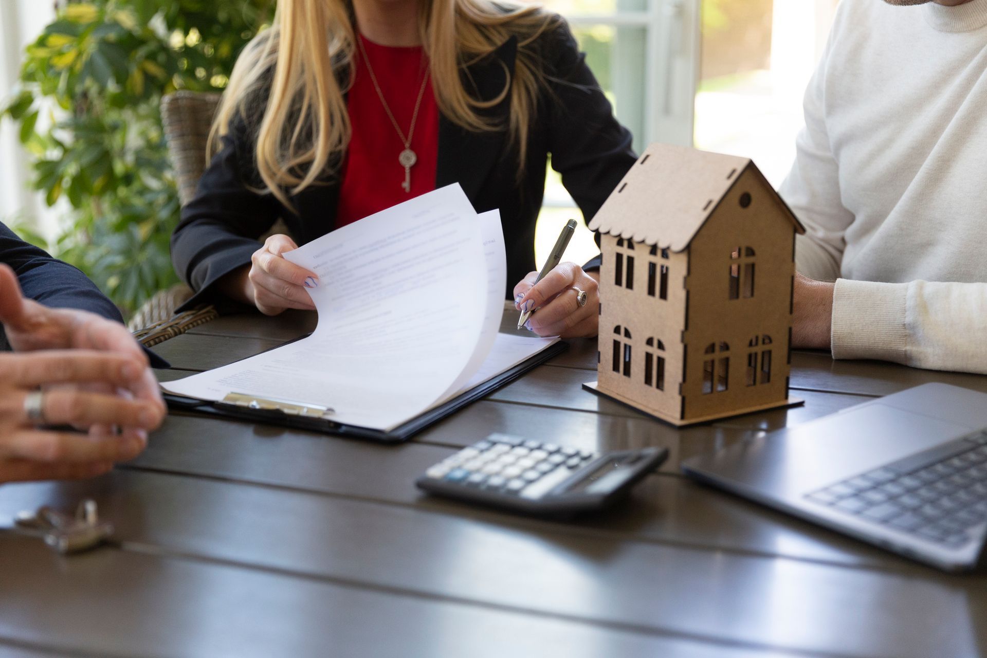 A woman is sitting at a table with a model house and a calculator.