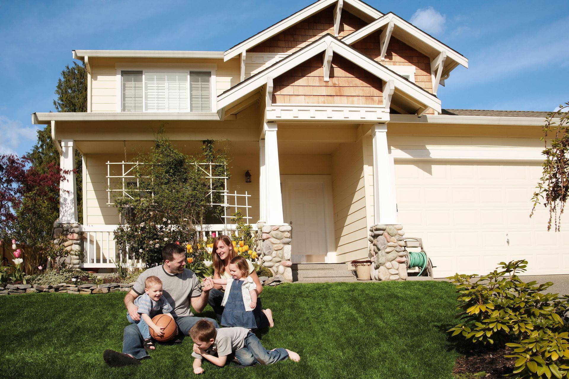 A family is sitting on the grass in front of a house.