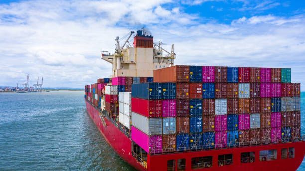 Red cargo ship sailing in ocean, carrying stacks of shipping containers.