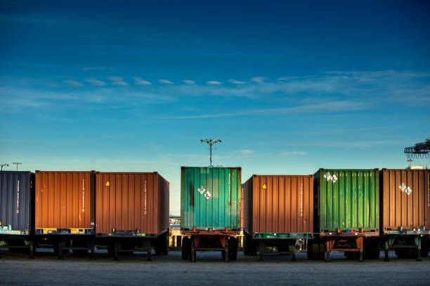 Shipping containers on trailers under a blue sky.