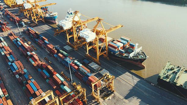 Aerial view of a cargo ship being loaded with shipping containers at a busy port with large cranes.