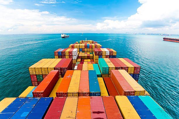 Cargo ship at sea, loaded with colorful shipping containers. Bright blue water, sky.