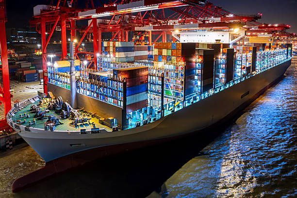 Cargo ship at a dock, illuminated at night with red cranes loading shipping containers.