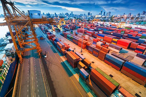 Shipping port with cargo containers, crane, and city skyline in the background.