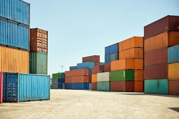 Shipping containers stacked in a yard, various colors, under a blue sky.