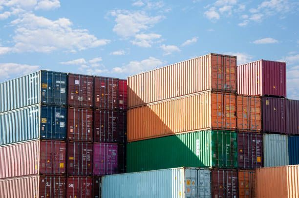 Stacks of colorful shipping containers against a blue sky with fluffy clouds.