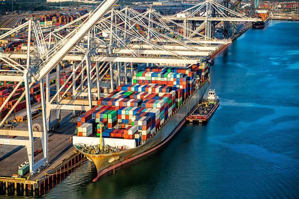 Cargo ship docked at port, loading containers, blue water, overhead cranes.