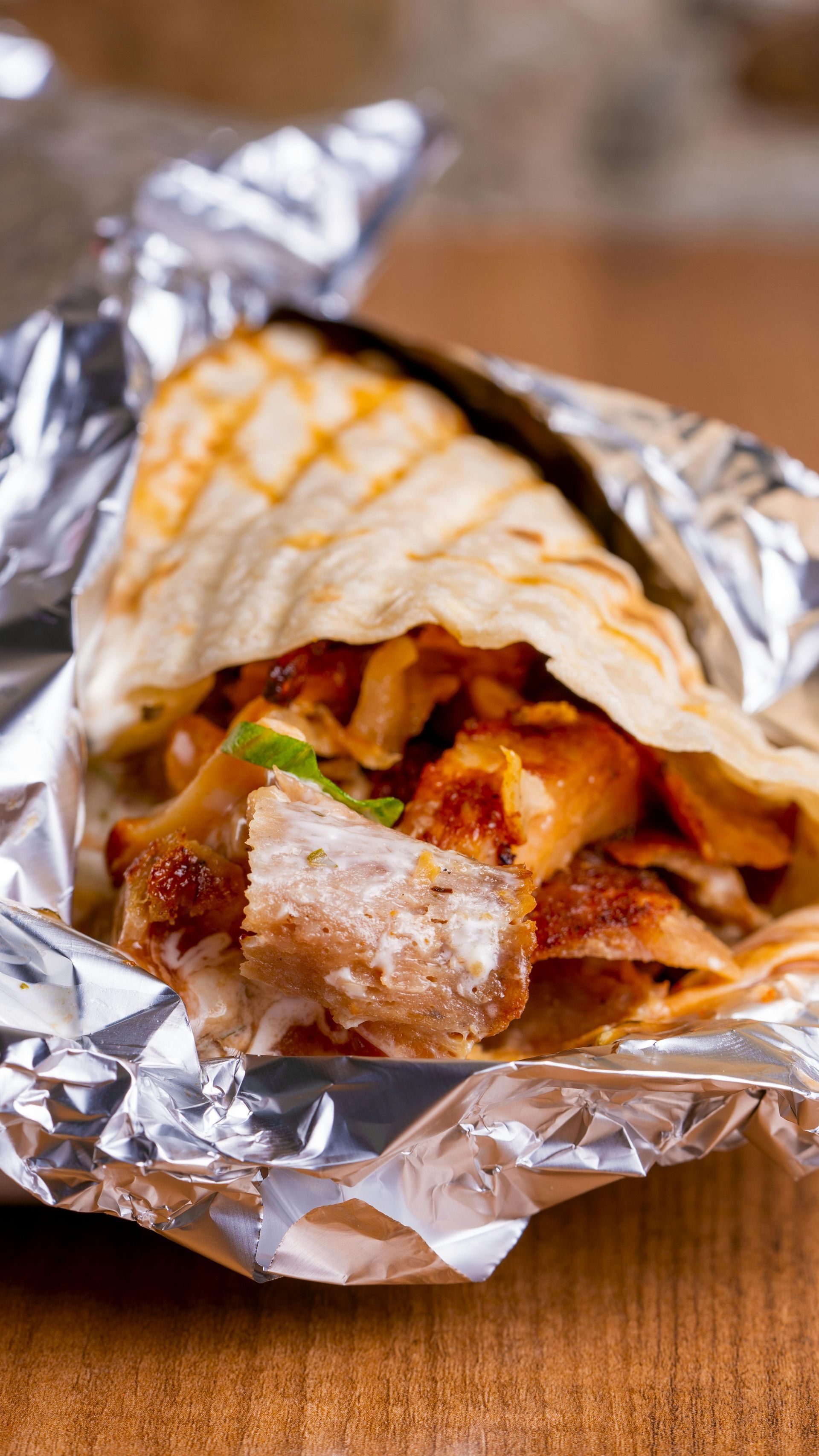 Taco wrapped in foil, showing grilled meat and onions.