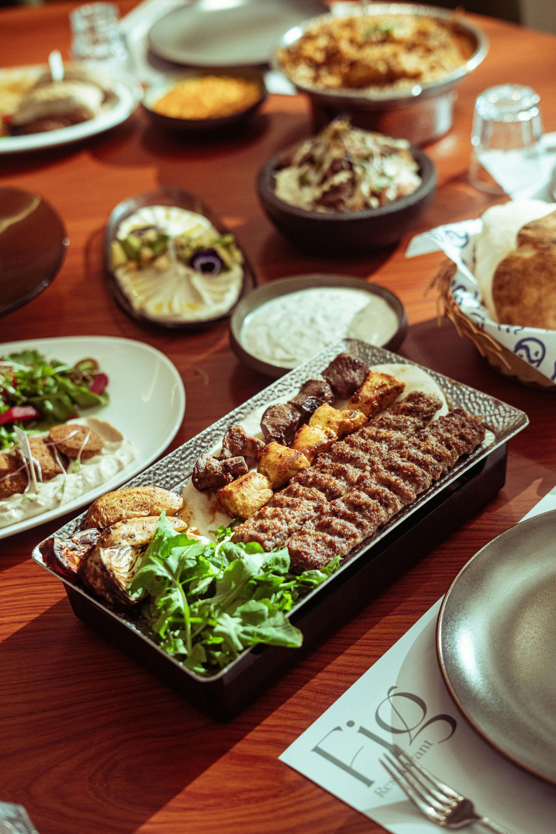 Table set with various Middle Eastern dishes, including grilled meats, salads, and dips.