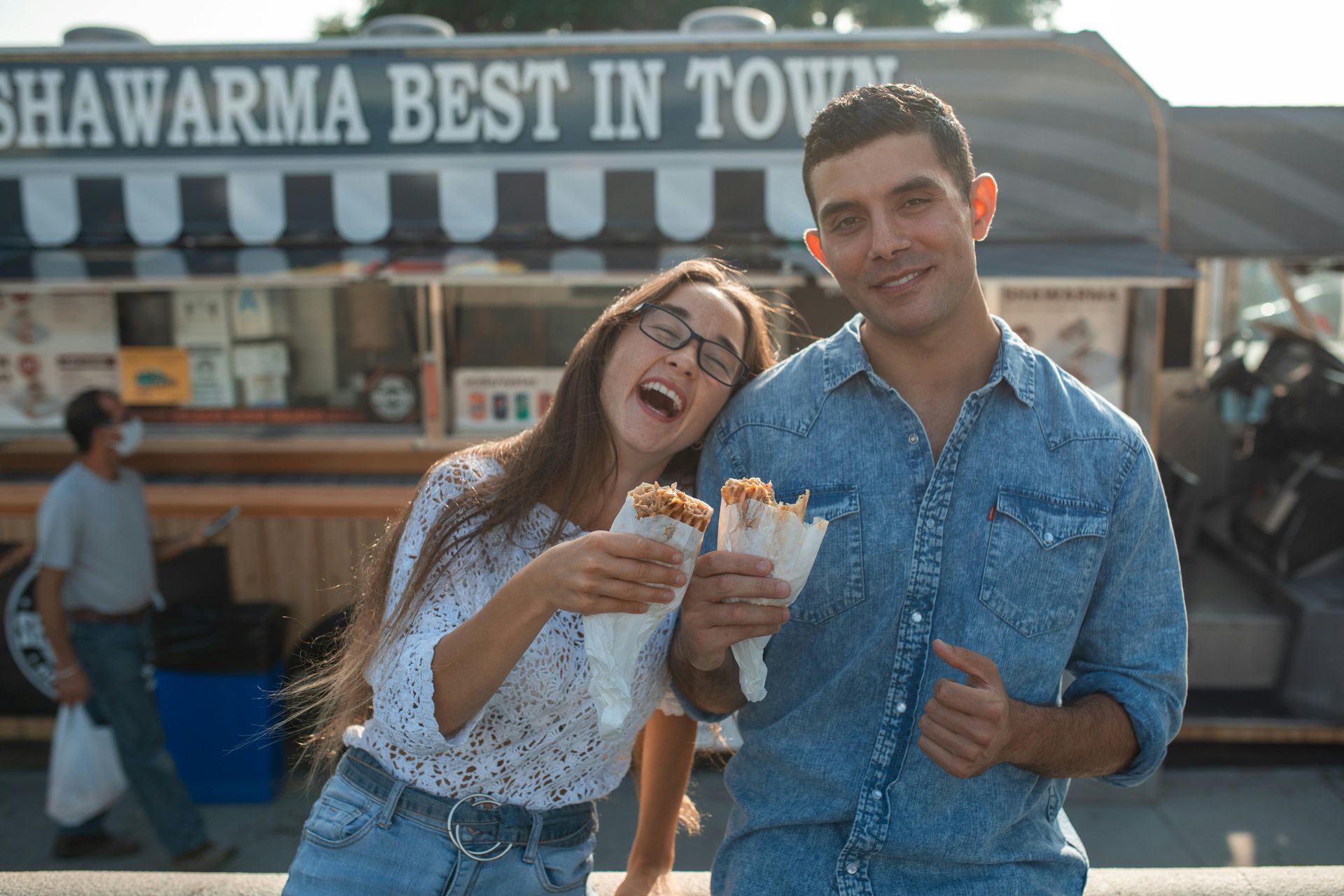 Couple laughing, holding shawarma in front of 