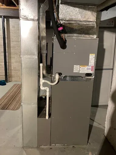Furnace unit with ductwork in a basement. Gray metal with white PVC pipes.