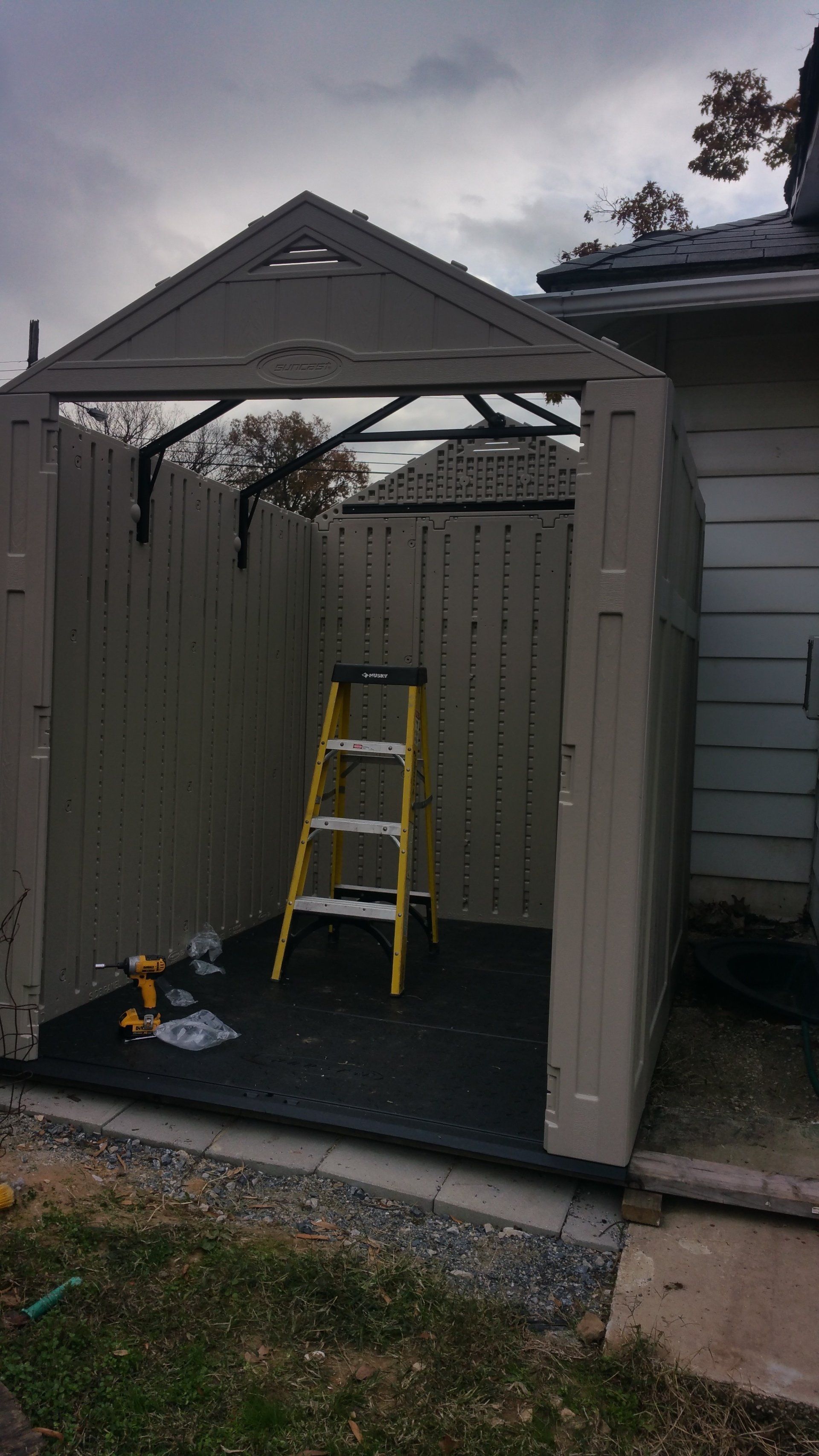 A ladder is sitting inside of a shed next to a house.