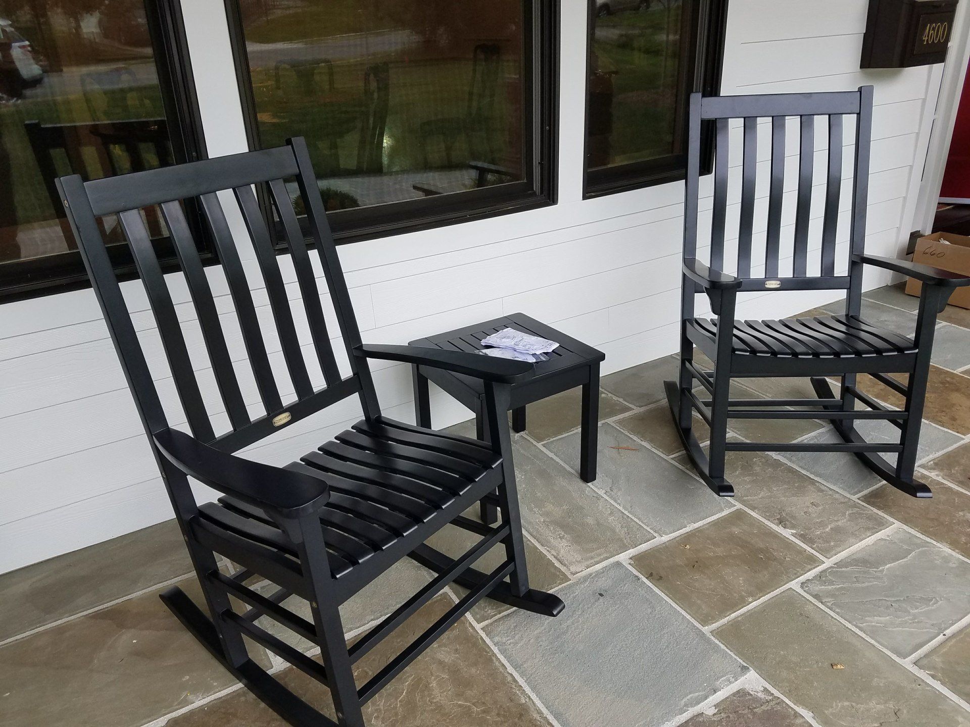 Two black rocking chairs and a small table on a porch.