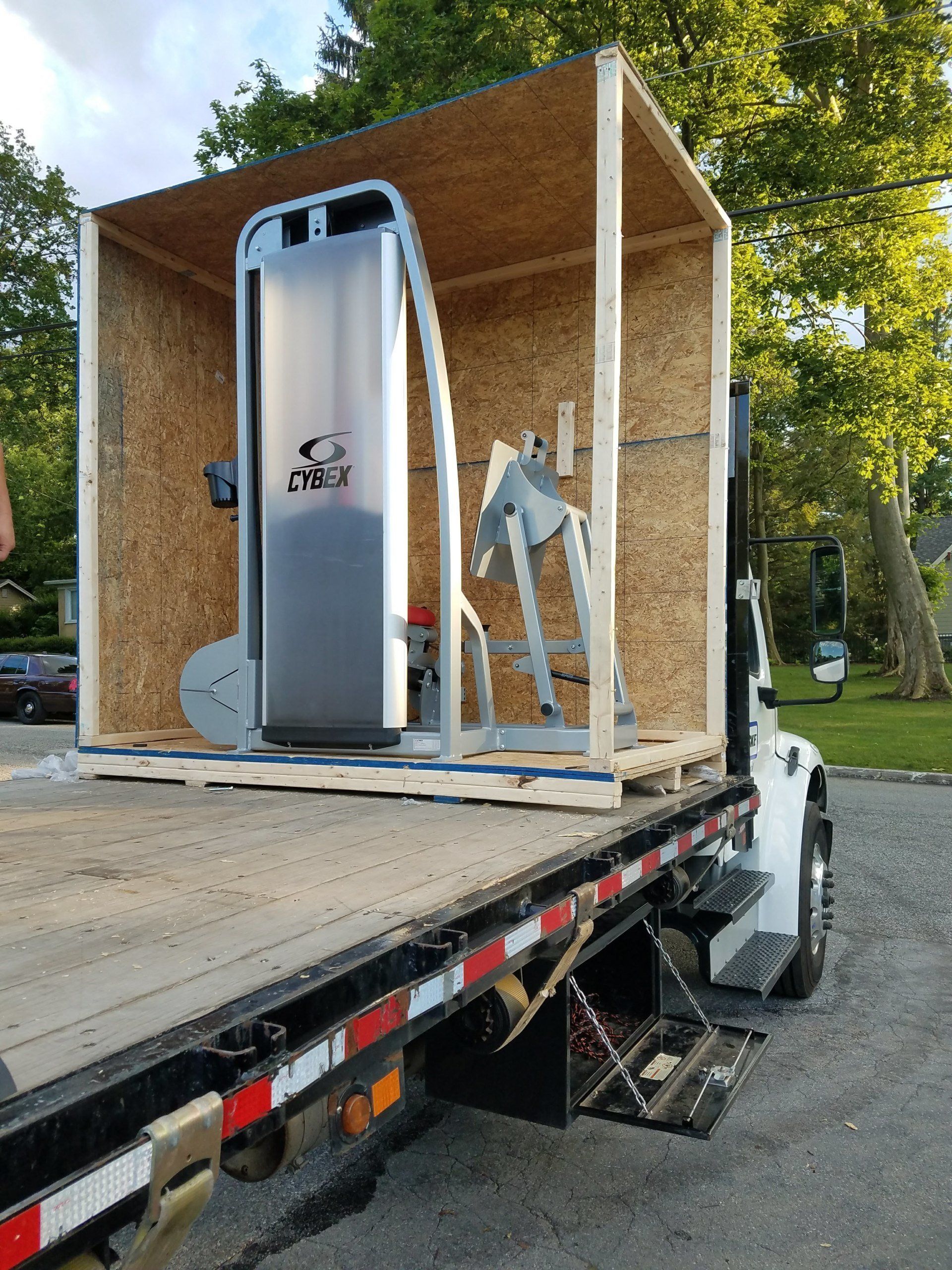 A gym machine is in a wooden crate on the back of a tow truck