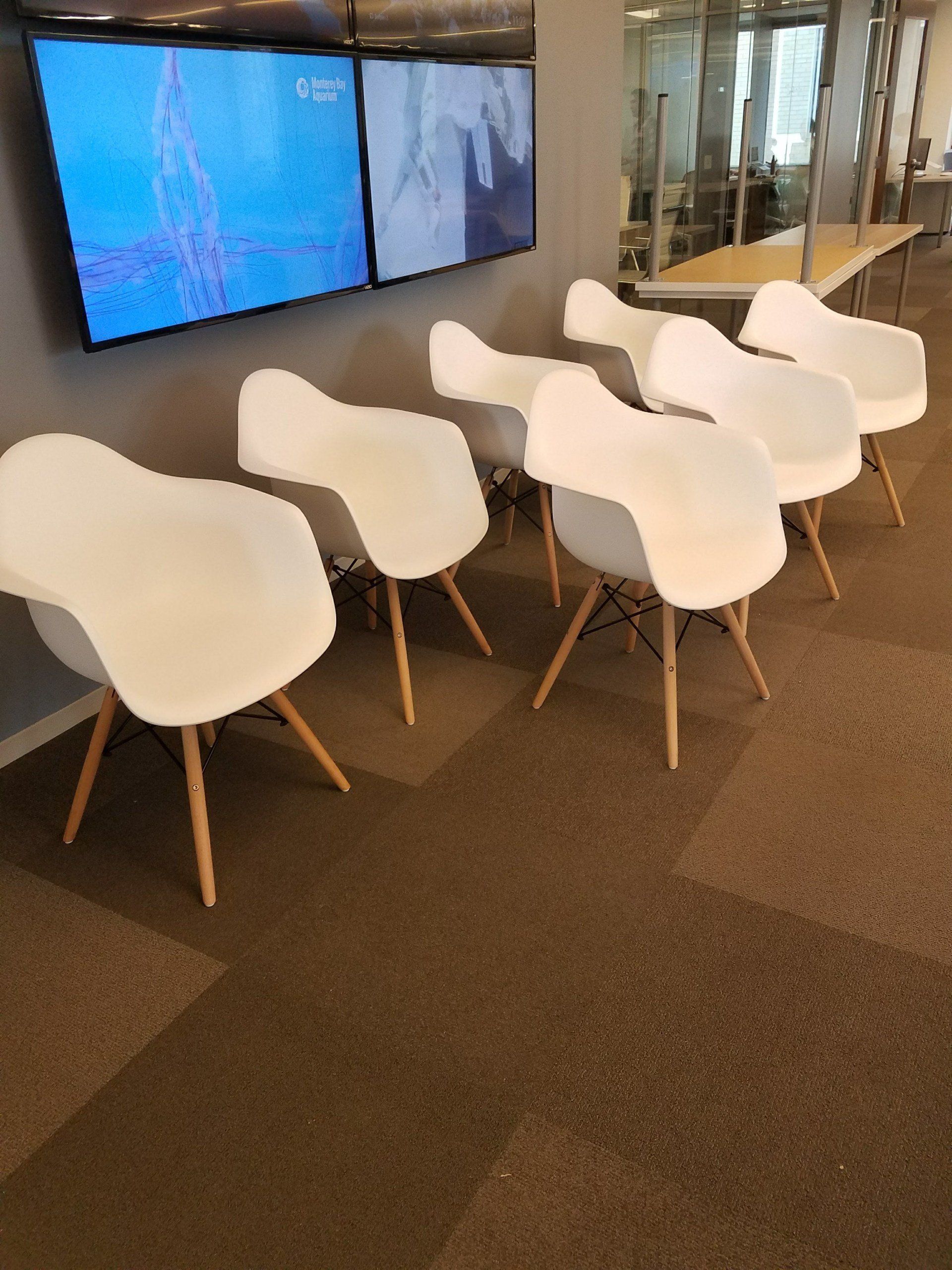 A row of white chairs in a room with a tv on the wall