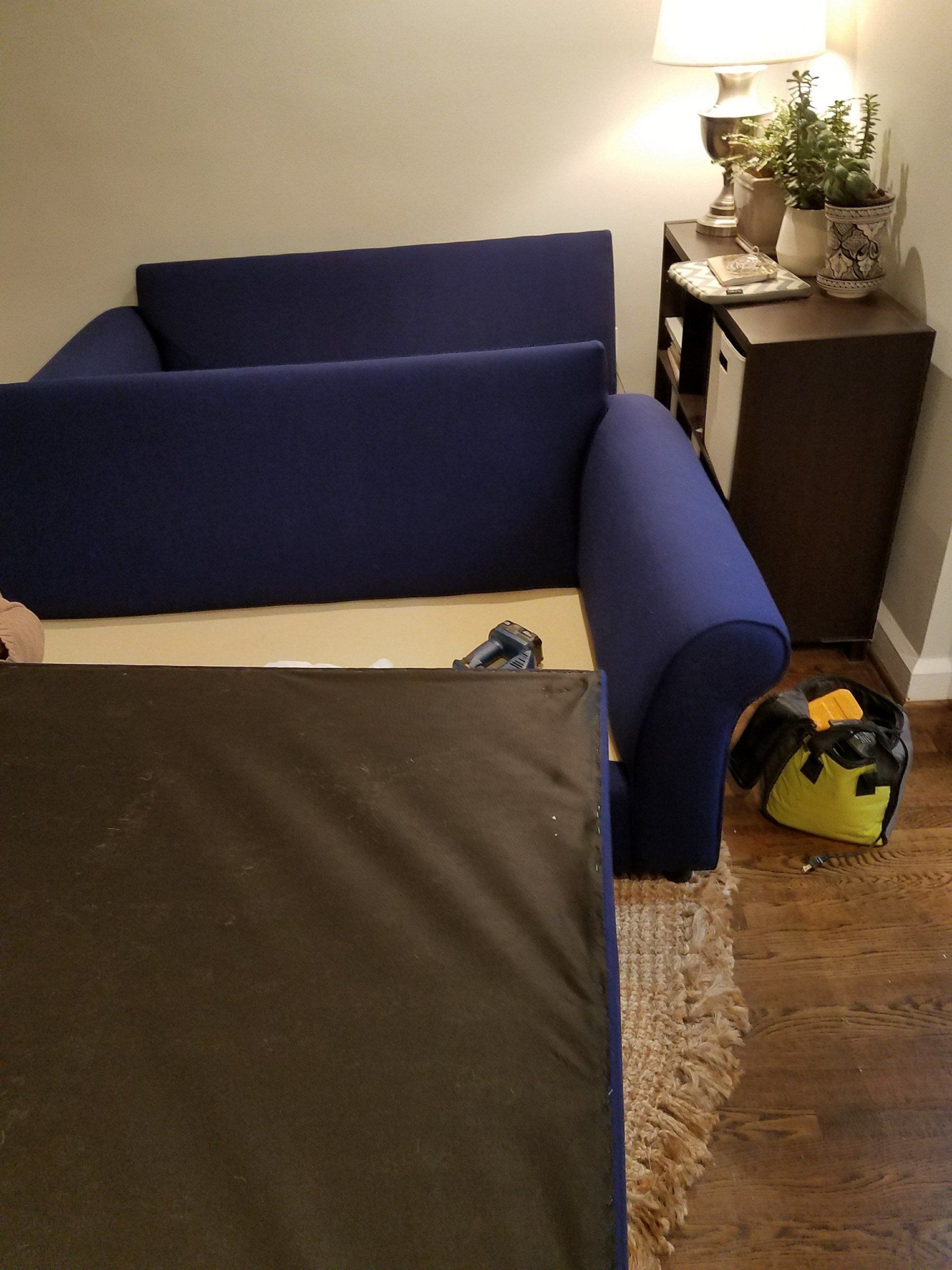 A blue couch is sitting in a living room next to a yellow vacuum cleaner.