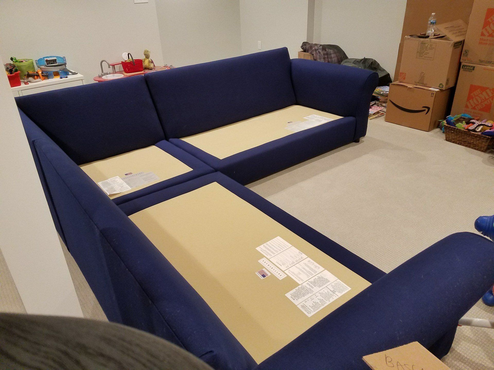 A blue sectional couch is sitting in a room with boxes on the floor